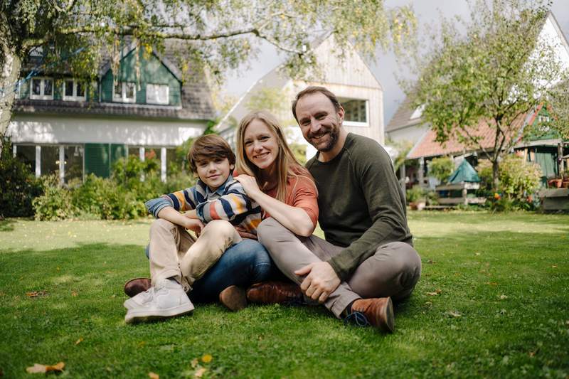 Parents and boy sit on lawn in front of a home.