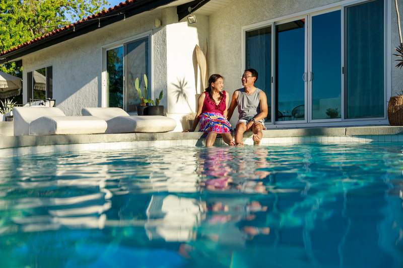 Woman and man sit on edge of pool at a vacation rental.
