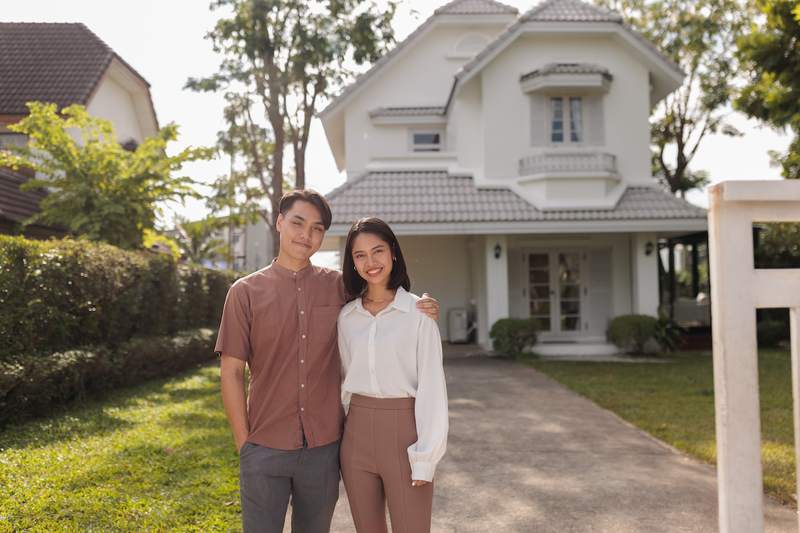 A smiling man and woman pose in front of their new home.