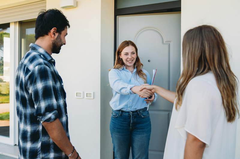 Agent and couple shake hands at front door of a home.