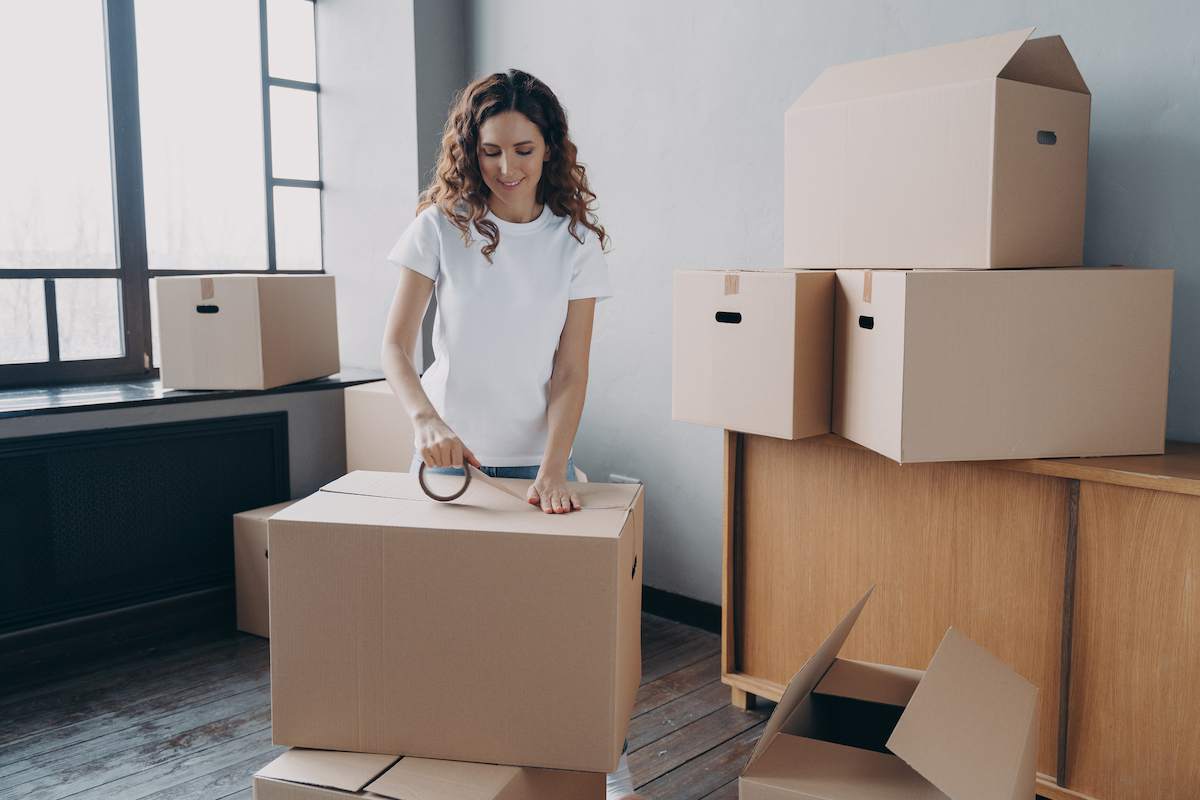 A woman packs moving boxes in an apartment.