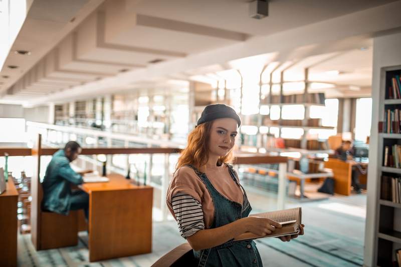 Person with student loan debt checking out a book in a library.