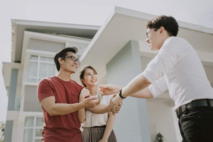 A couple shakes hands with a real estate agent outside a home.