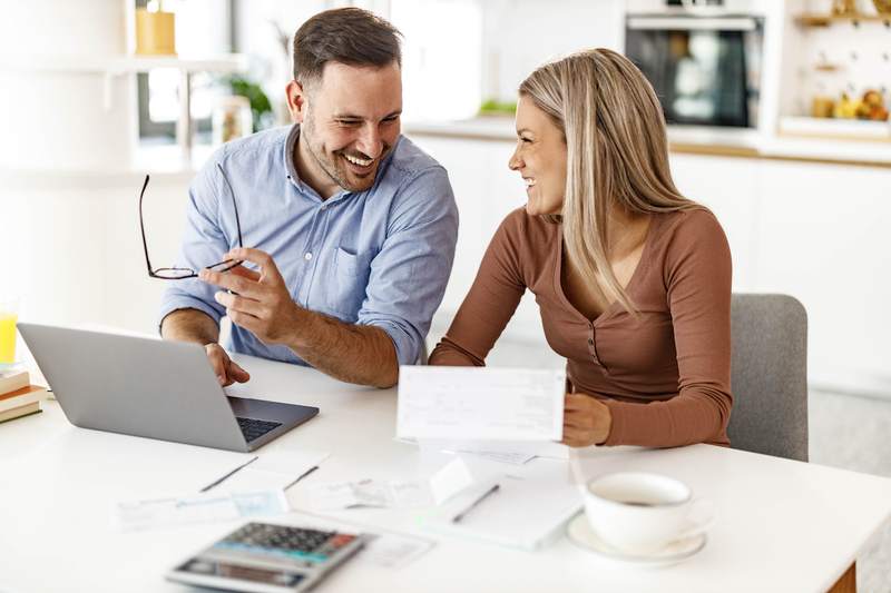 A happy man and woman discuss finances at a table with a laptop.