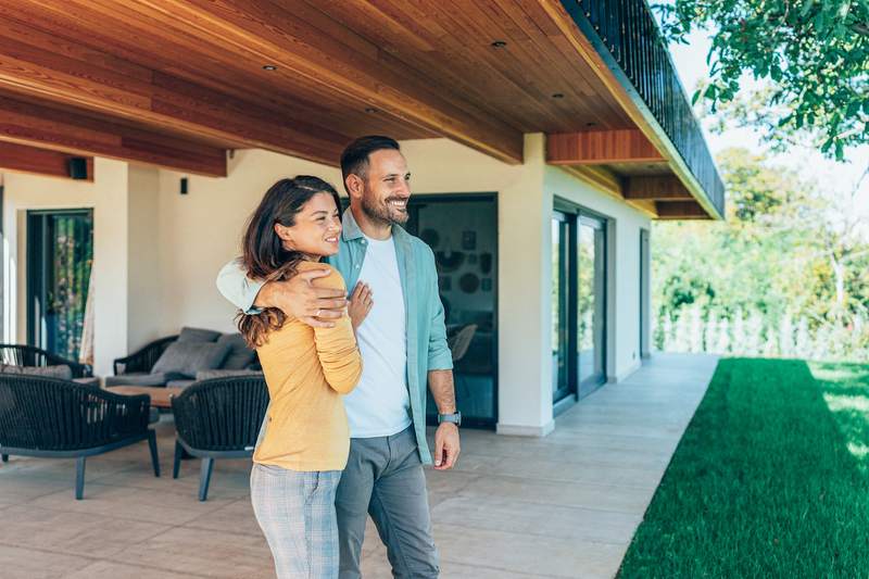 A man and woman embrace on the porch of their new home.