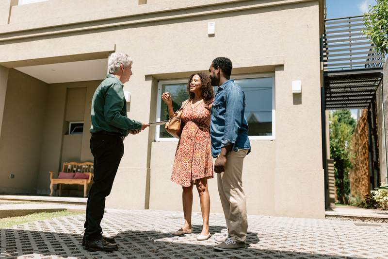 White real estate agent shows home for sale to a Black couple.