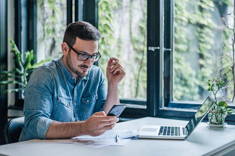 Man checks finances on his phone and laptop.