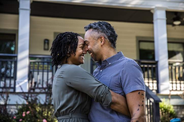 A couple embraces in front of a home.