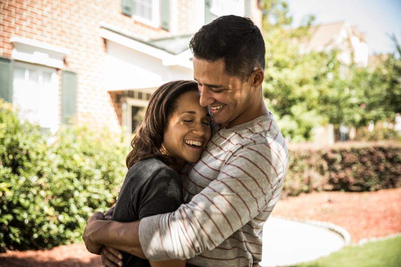 Happy couple hugs outside a home.