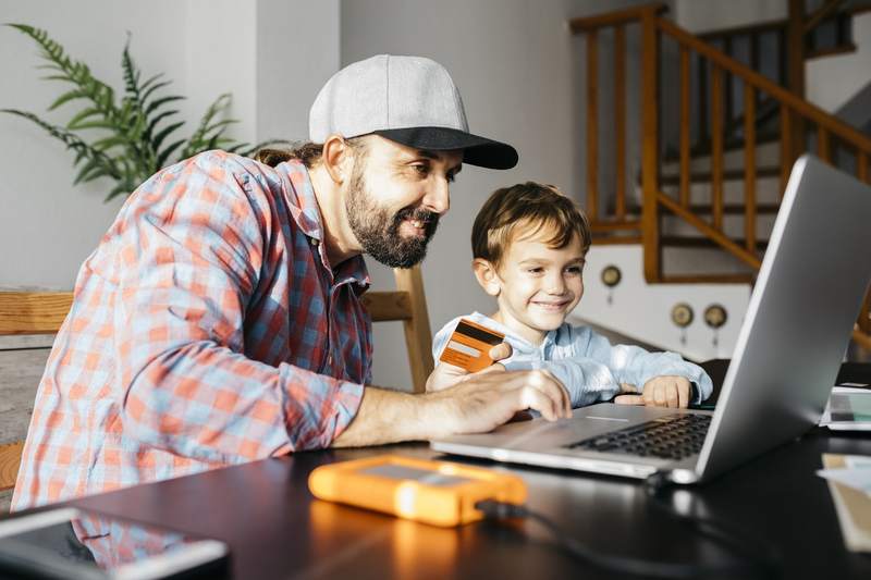 A father, with a child by his side, looking at a laptop computer to check his credit score.