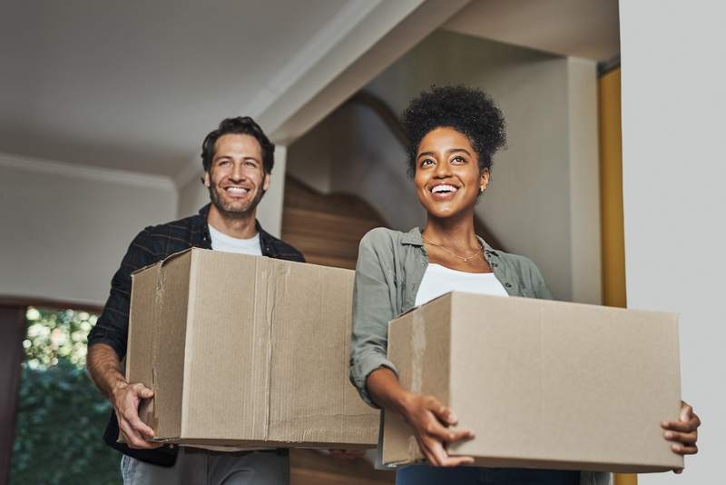 A smiling couple carries boxes into their new home.