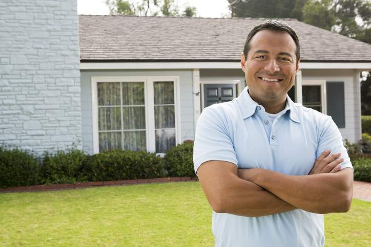 Man stands proudly in front of his home.