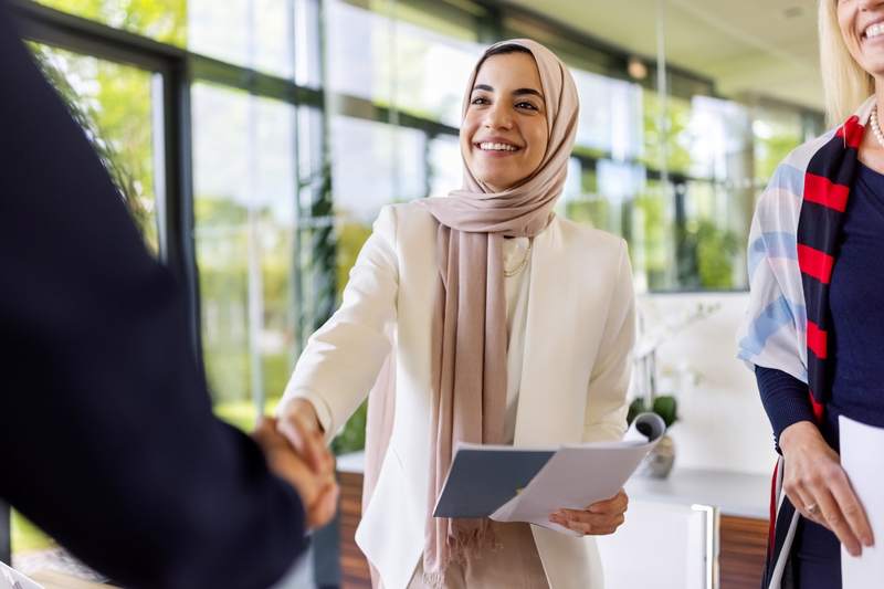 Woman with papers shakes agent's hand in an office setting.