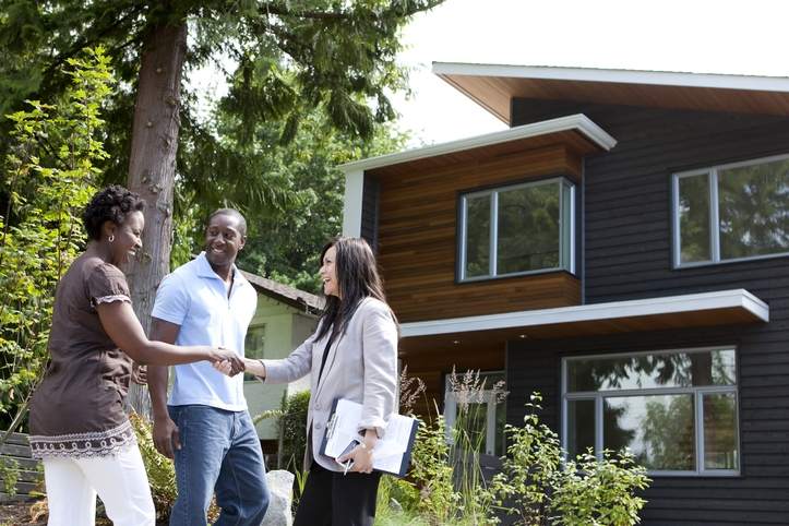 Black couple meets real estate agent outside home.
