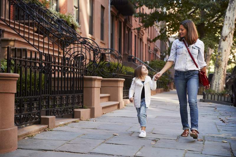 A mother and daughter take a walk in a brownstone neighborhood.