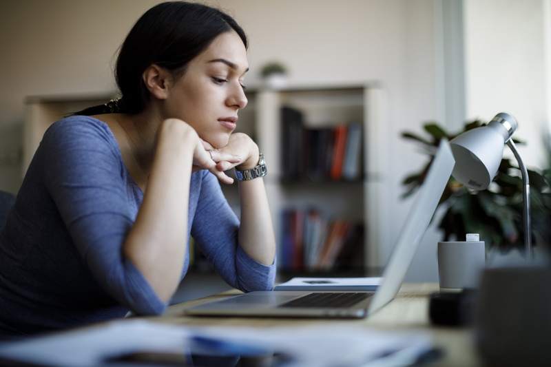 A woman waits in front of her laptop with her hands underneath her chin, looking for updates on her mortgage refinance application.