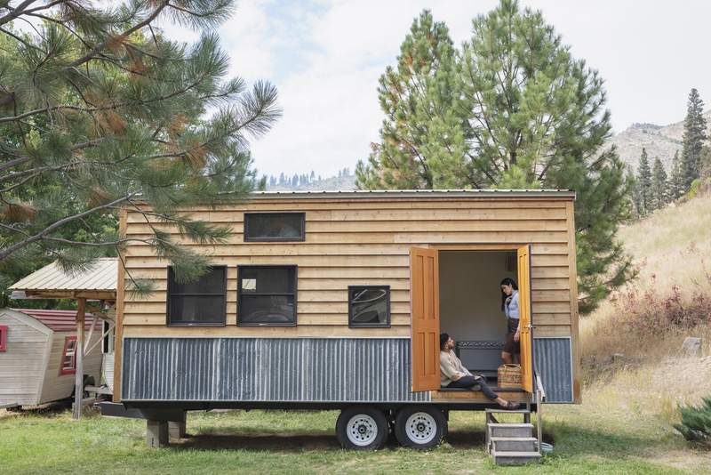 A couple relaxes in the doorway of a mobile tiny house.