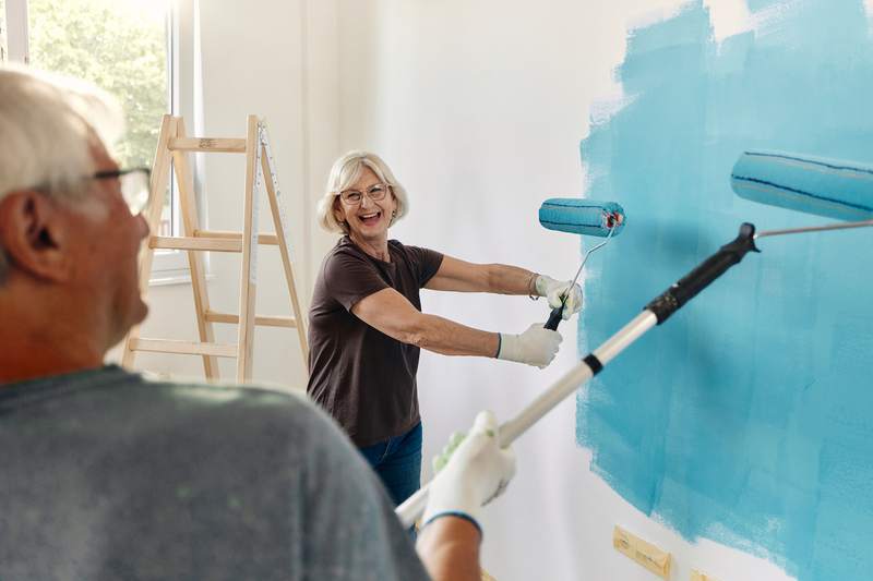 An older man and woman paint the walls of a living space.